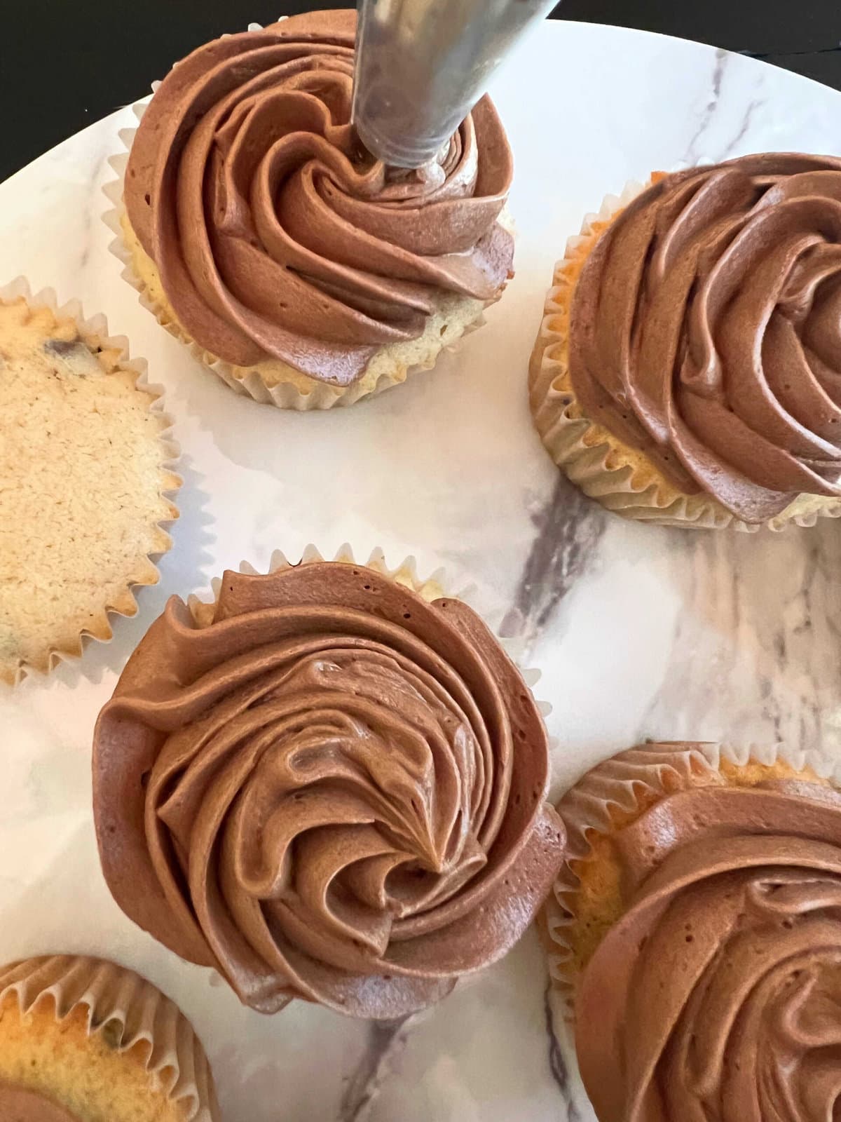 Piping chocolate swirls onto cooled chocolate chip cupcakes.