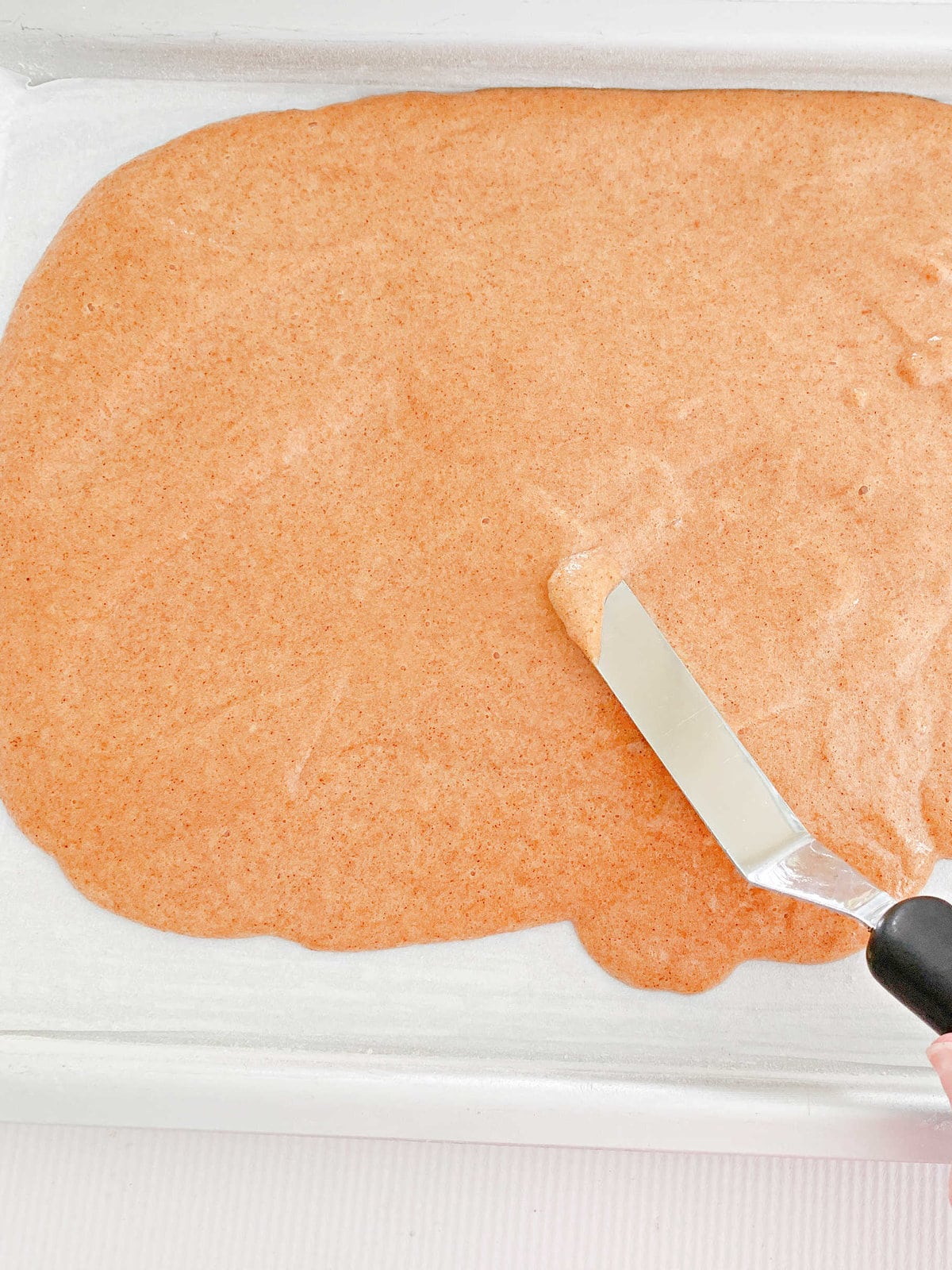 Spreading pumpkin roll batter into parchment lined sheet pan.