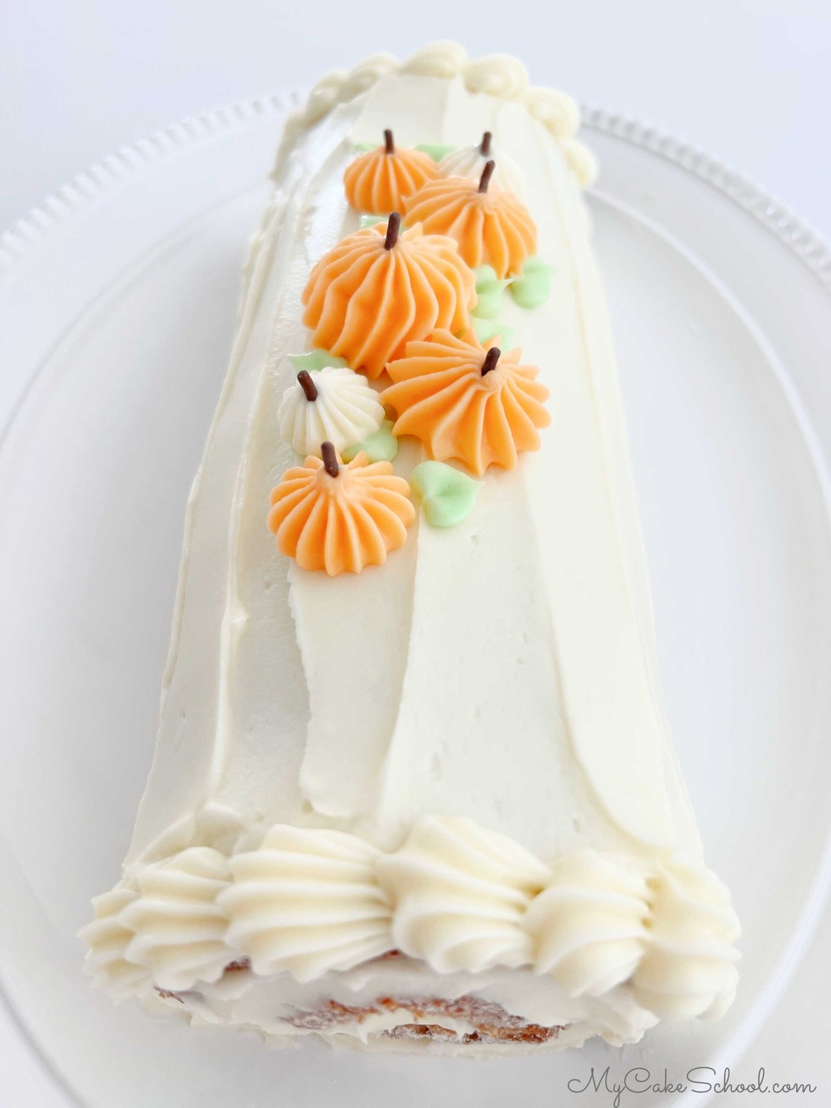 Pumpkin Roll Cake frosted with cream cheese frosting and topped with piped frosting pumpkins.