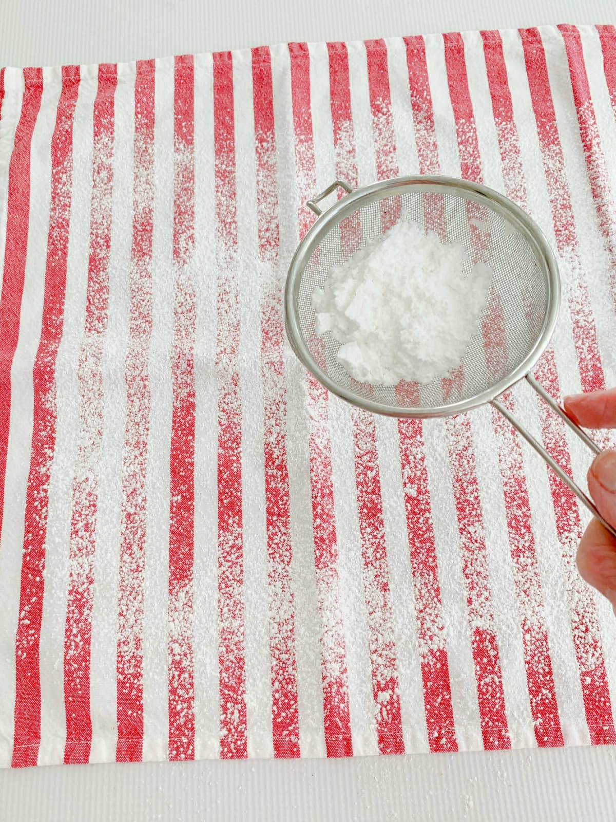 Dusting clean towel with powdered sugar for pumpkin roll cake.