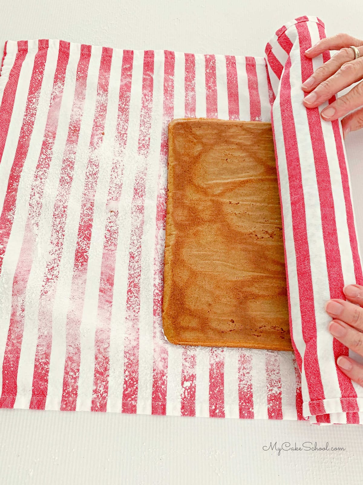 Rolling up the pumpkin cake layer in a sugared dish dowel.