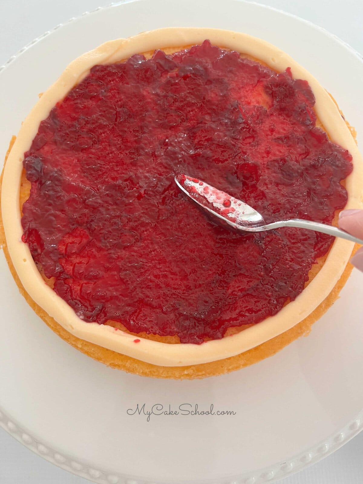 Spreading orange filling over the cranberry orange cake layer.