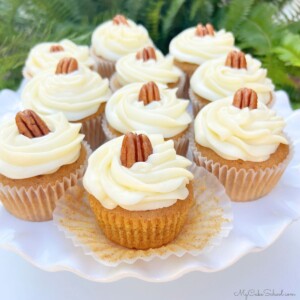 Cake pedestal filled with sweet potato cupcakes, topped with swirls of cream cheese frosting and pecans.