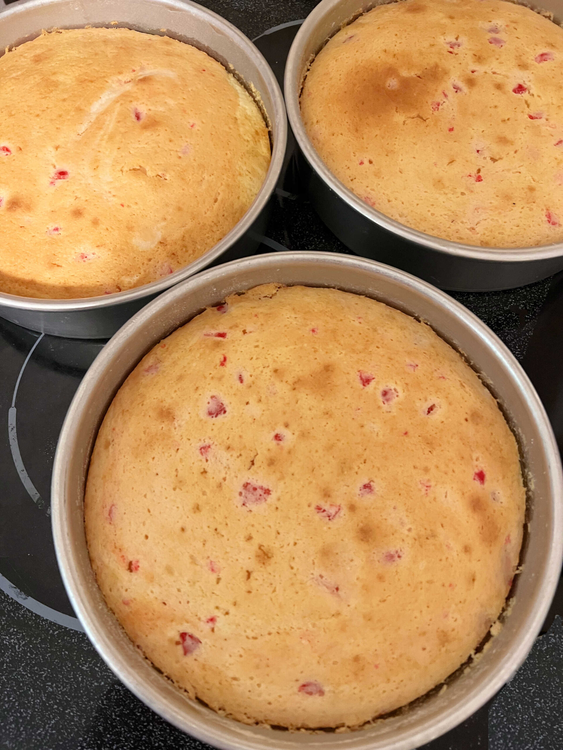 Freshly baked cherry almond cake layers, still in pans.