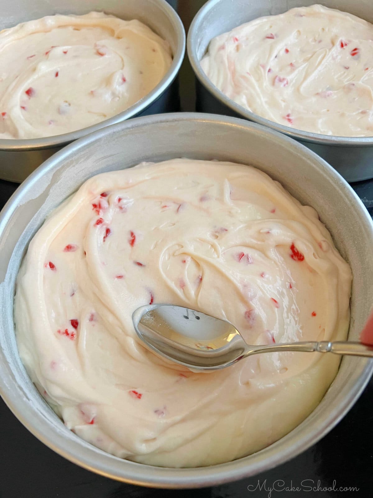 Smoothing Cake Batter into pans using the back of a spoon.