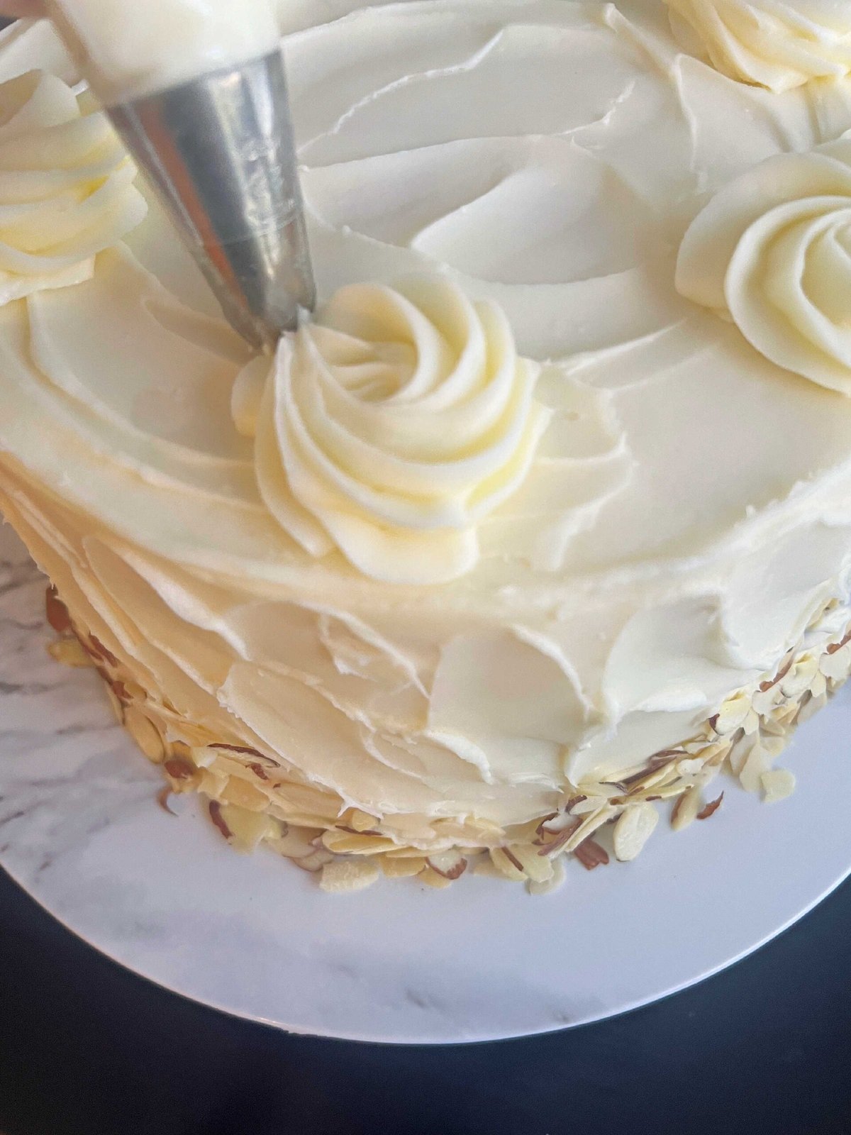 Piping swirls of frosting on top of the cake using a large 2D star tip.