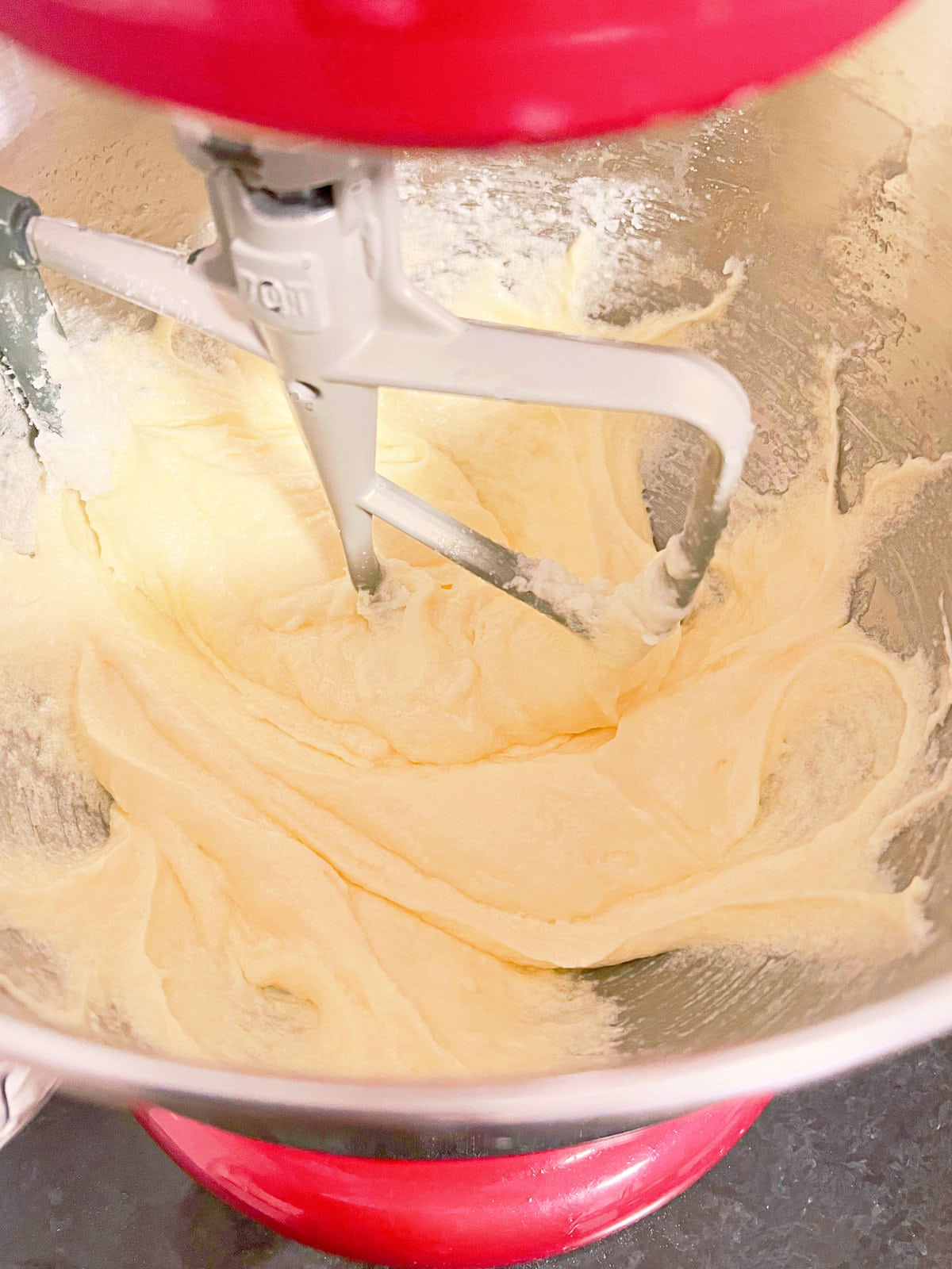 Adding eggs to butter and sugar mixture in mixing bowl.