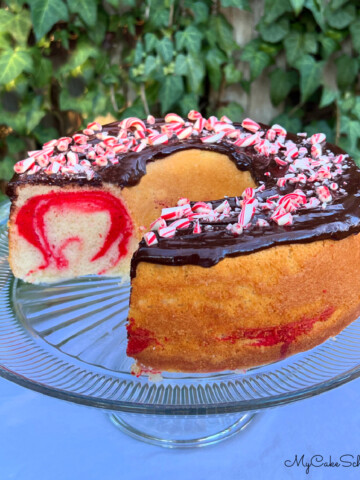 Sliced Peppermint Bundt Cake with red swirls. Topped with chocolate glaze and crushed candy canes.