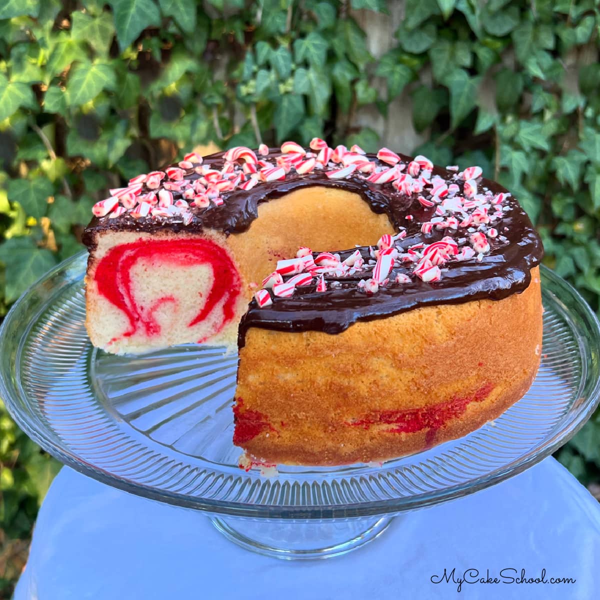 Sliced Peppermint Bundt Cake with red swirls. Topped with chocolate glaze and crushed candy canes.