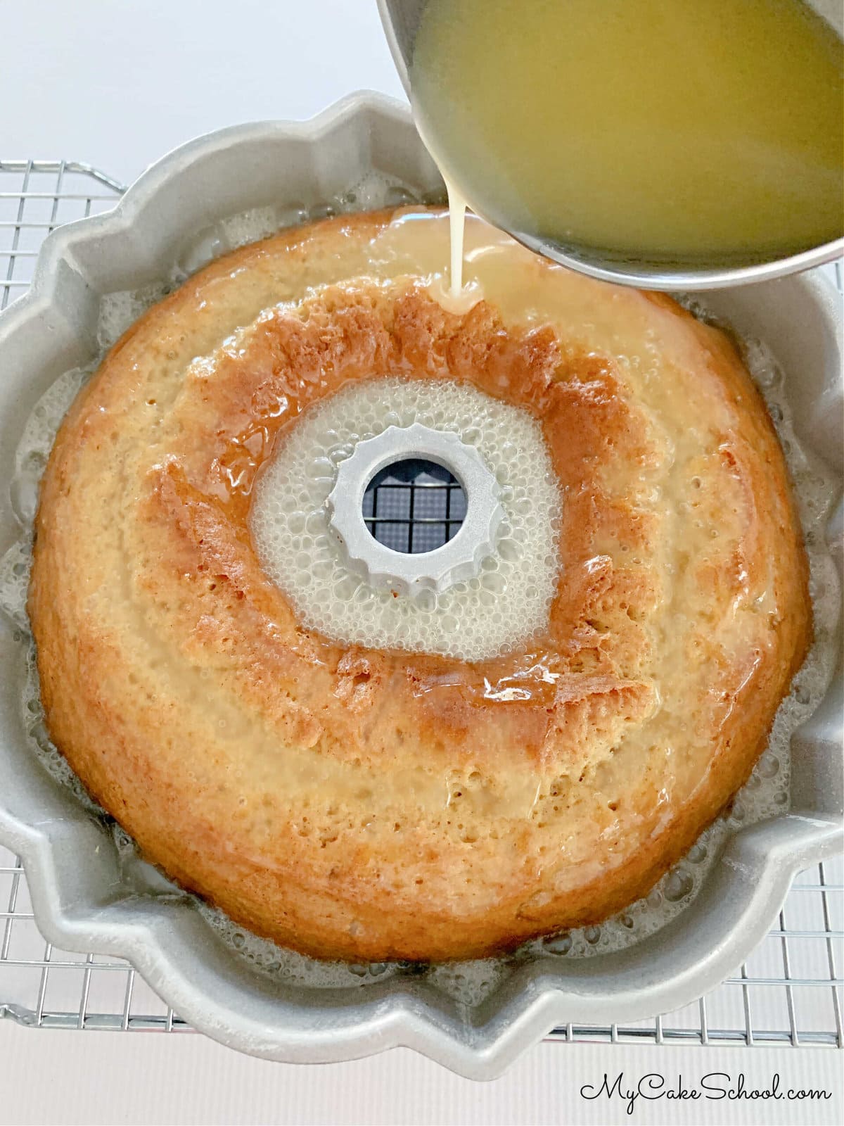 Pouring buttered rum glaze over the freshly baked cake, still in bundt pan.