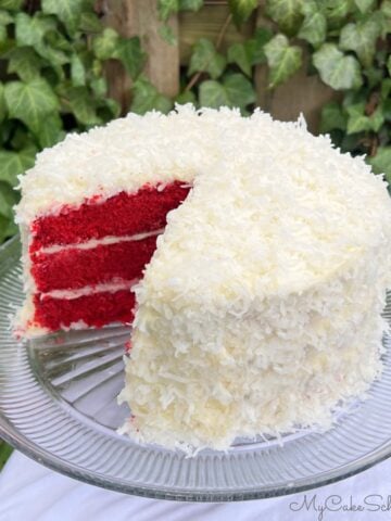 Sliced Red Velvet Coconut Cake on a glass cake pedestal.