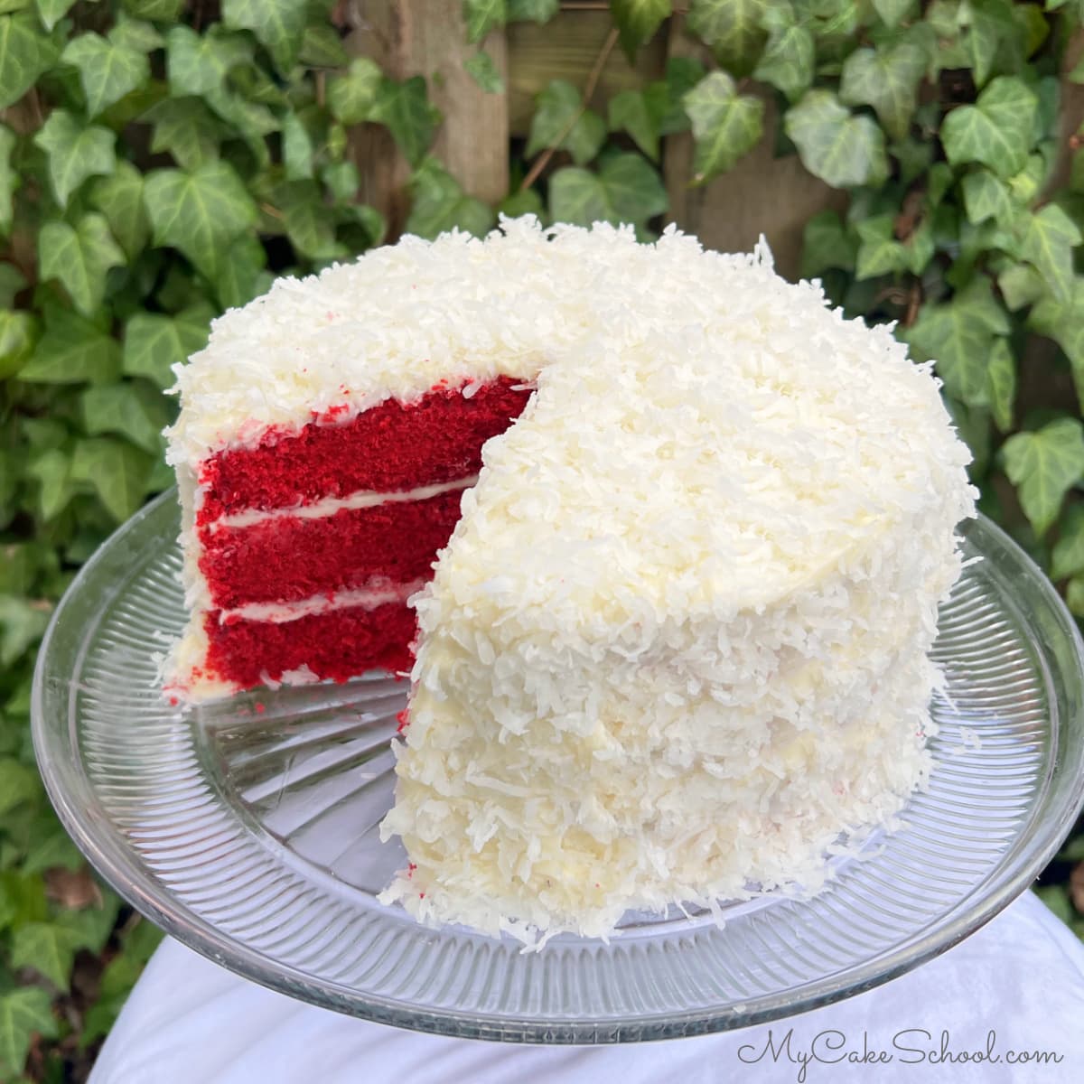 Sliced Red Velvet Coconut Cake on a glass cake pedestal.