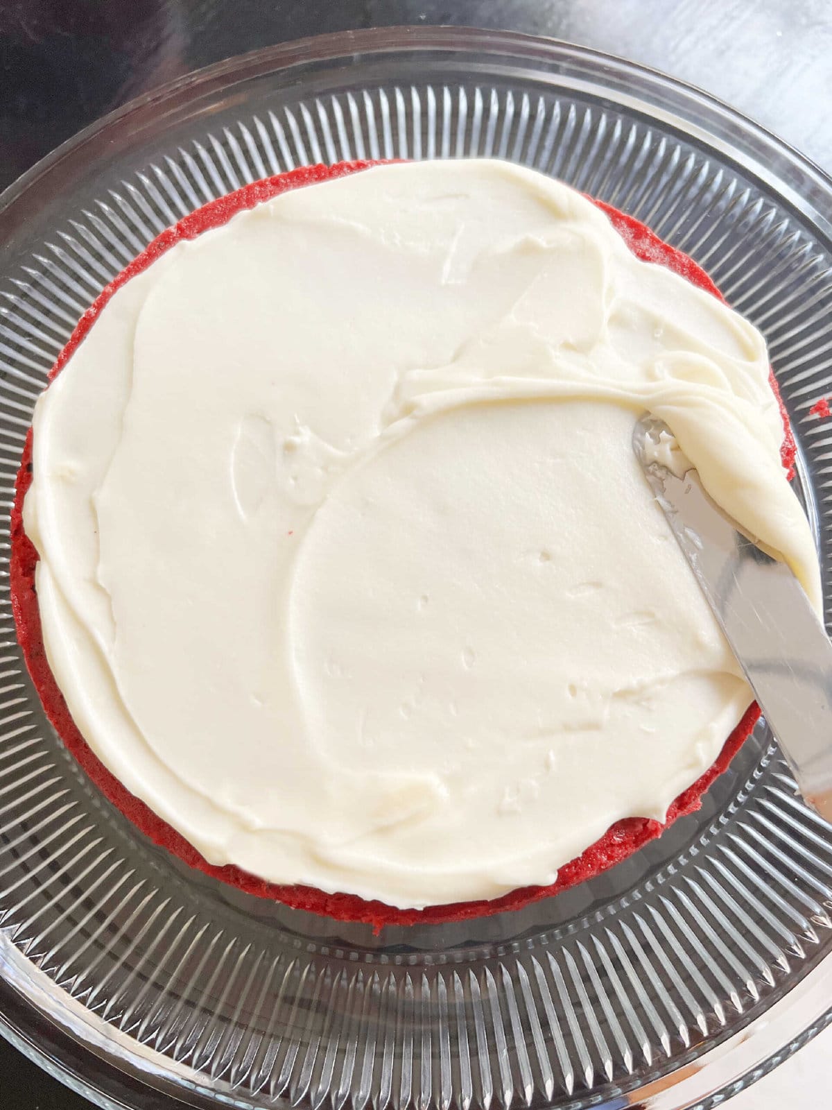 Spreading coconut cream cheese frosting onto red velvet cake.