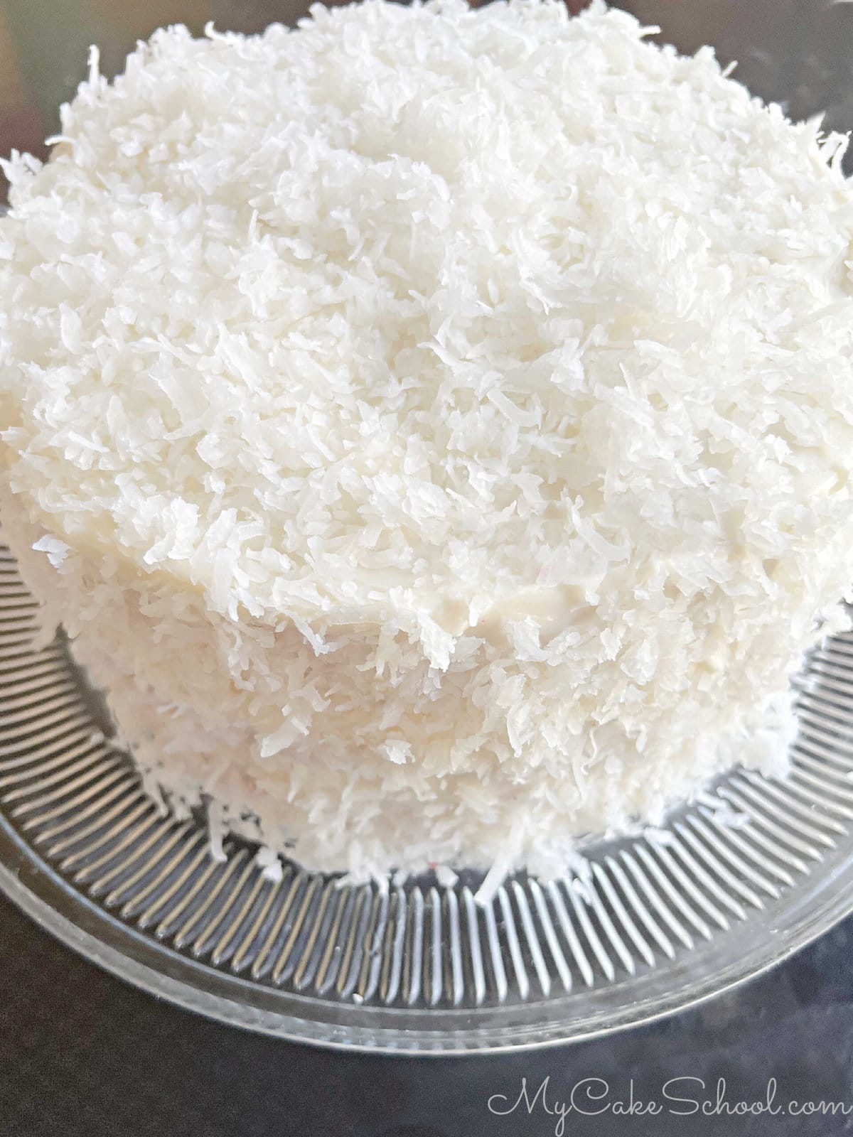 Red velvet coconut cake on a cake pedestal (before slicing). Cake is covered in shredded coconut.
