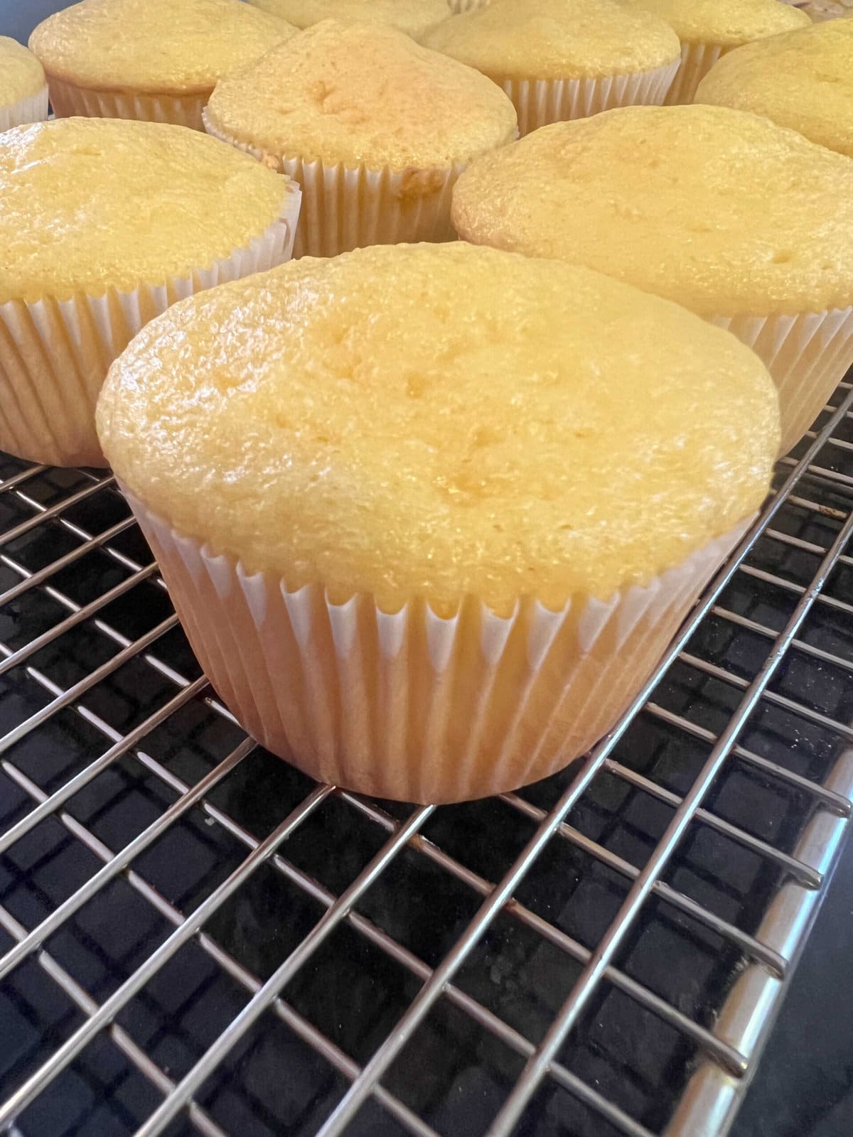 Yellow cupcakes, cooling on a cooling rack.
