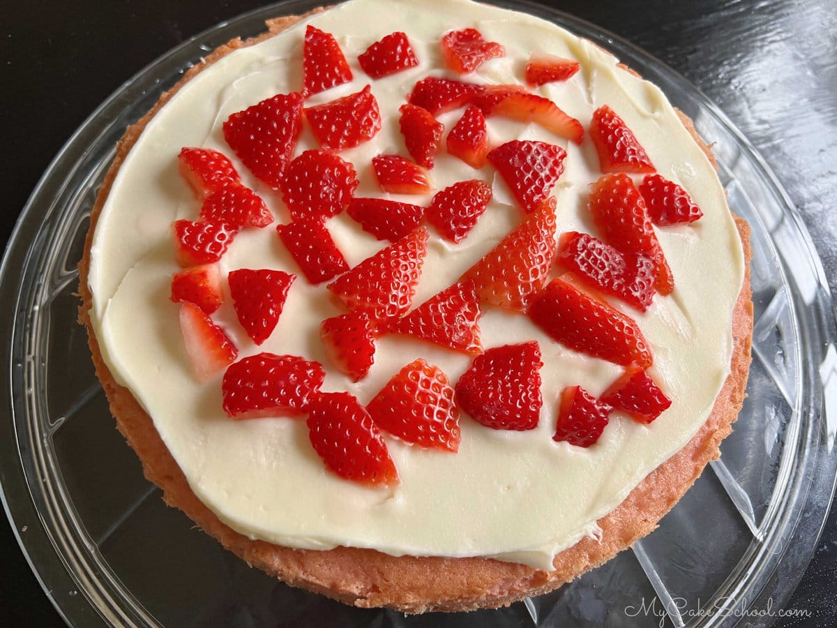 Sliced strawberries on top of frosted strawberry cake layer.