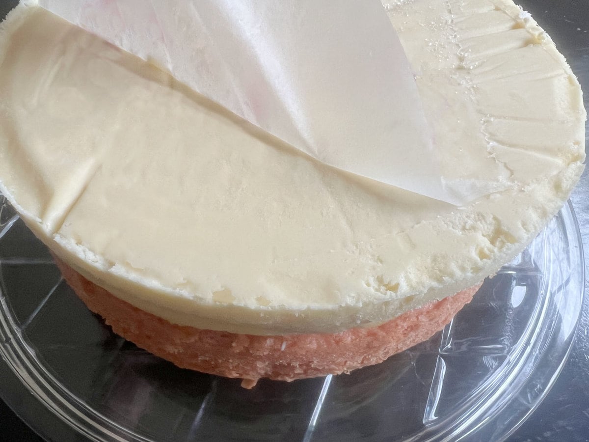 Peeling the parchment from the top of the cheesecake layer, after stacking on top of the strawberry cake layer.