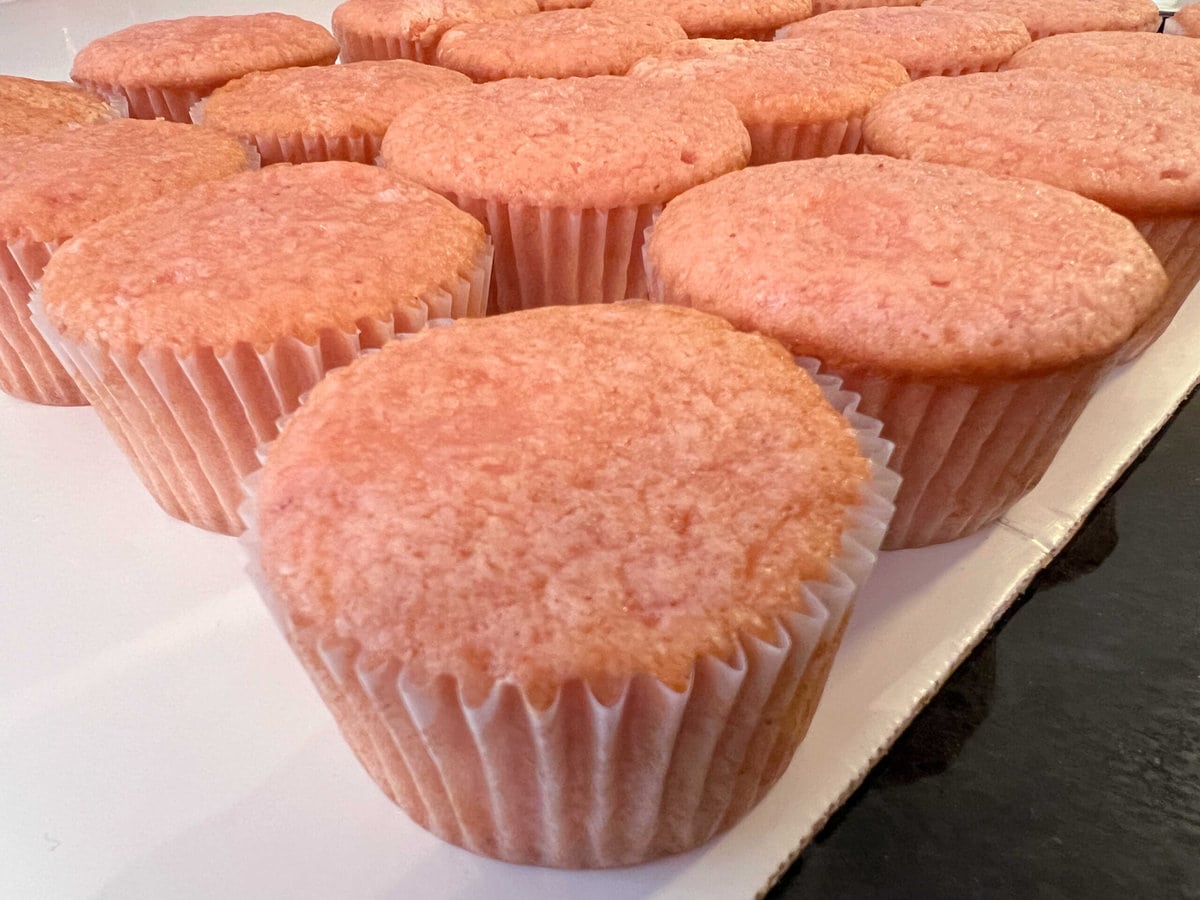 Freshly baked cupcakes on a cake board.