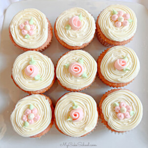 Closeup of 9 frosted strawberry cupcakes, topped with simple buttercream flowers and ribbon roses.
