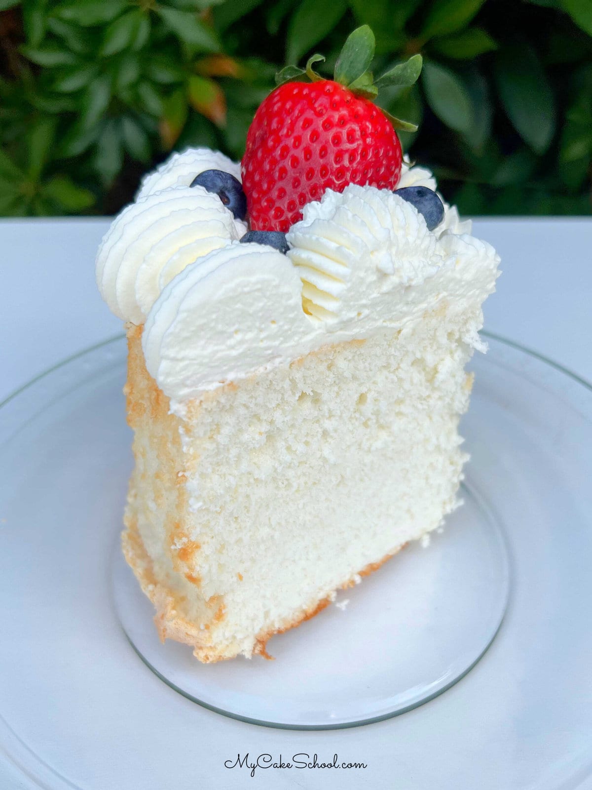 Slice of Angel Food Cake on a plate, topped with whipped cream and berries.