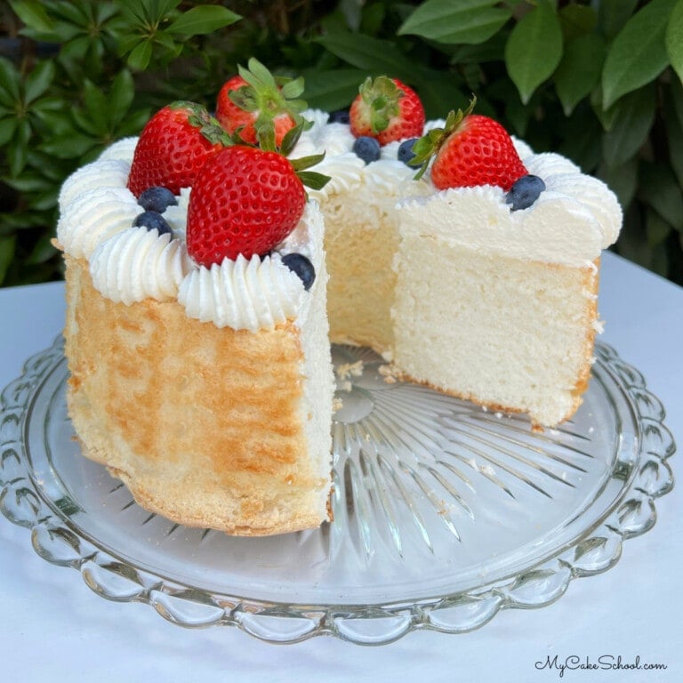 Angel Food Cake, sliced, on cake pedestal topped with berries and cream.