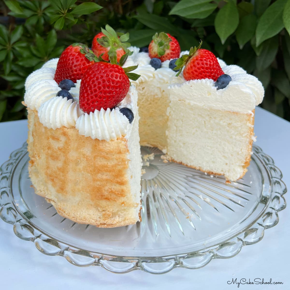 Angel Food Cake, sliced, on cake pedestal topped with berries and cream.