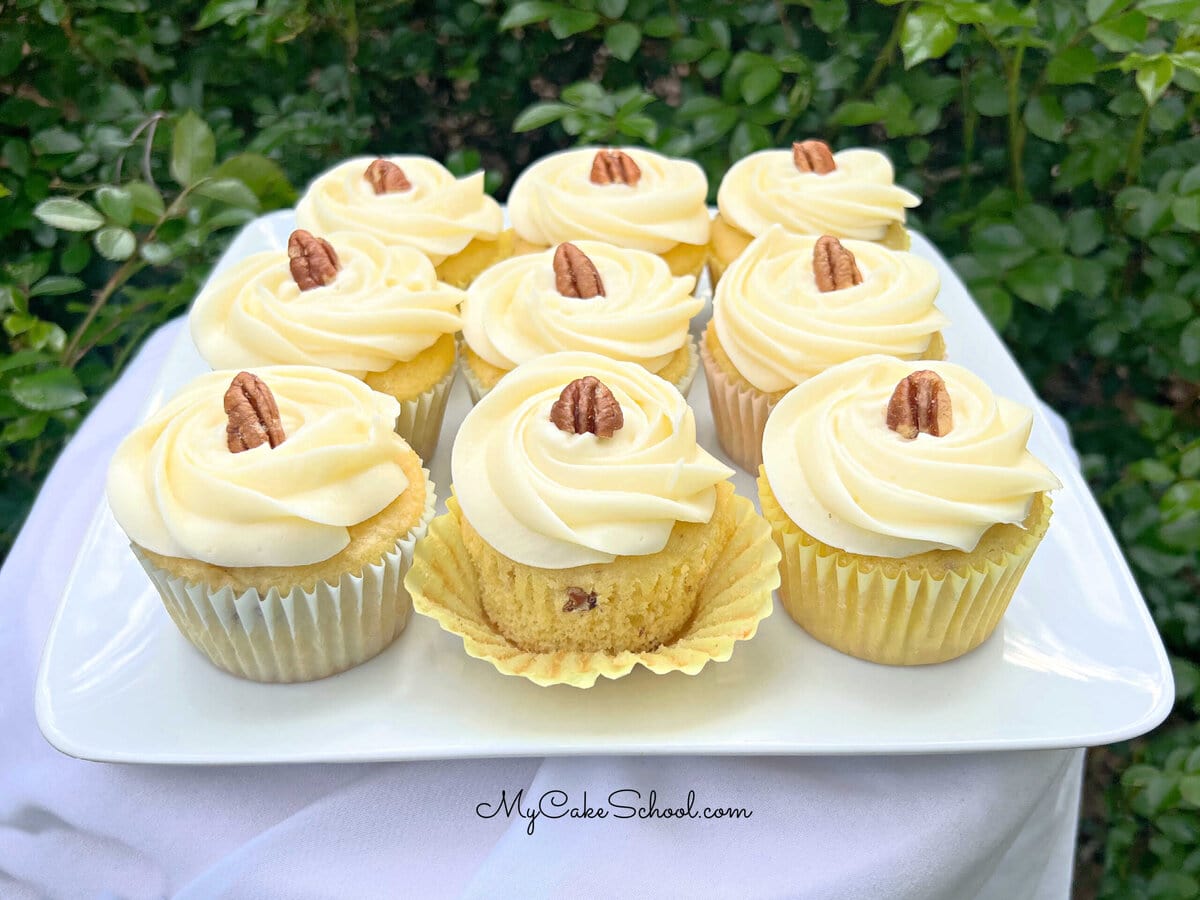 Italian Cream Cupcakes on a platter, swirled with cream cheese frosting and topped with pecans.
