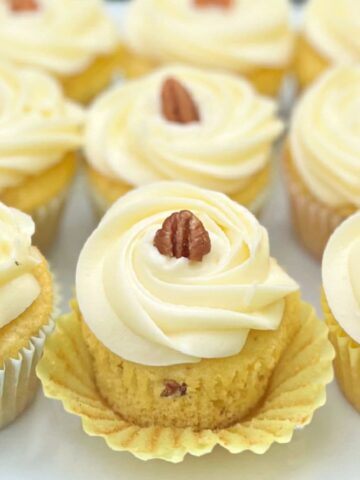 Italian Cream Cupcakes on a platter, swirled with cream cheese frosting and topped with pecans.