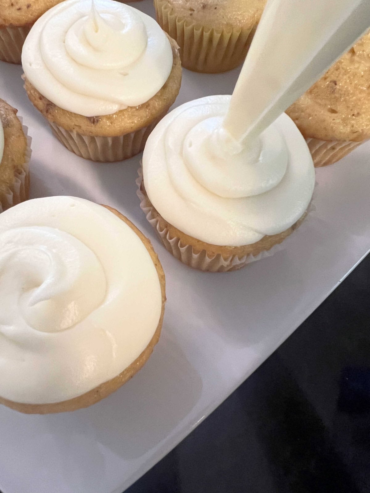 Piping swirls of cream cheese frosting onto the cupcakes.