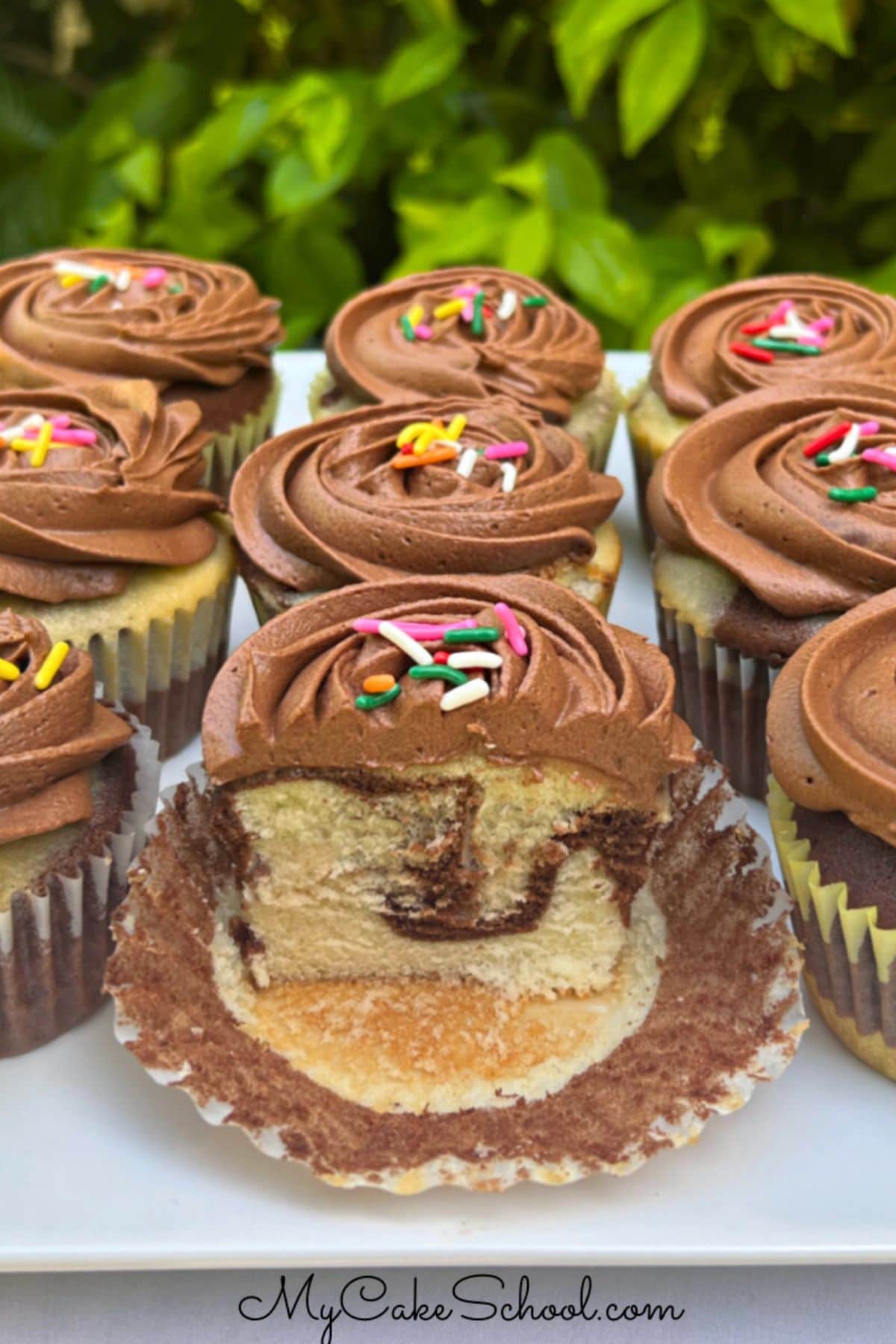 Marble Cupcakes on a cake platter, topped with chocolate frosting and colorful sprinkles.