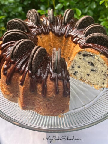 Oreo Pound Cake, topped with chocolate glaze and Oreos, on a cake pedestal.