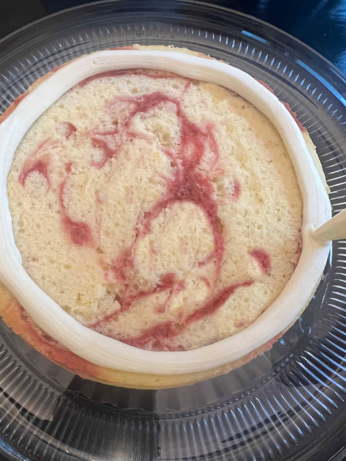 Piping a dam of frosting around the edge of the lemon raspberry swirl cake layer.
