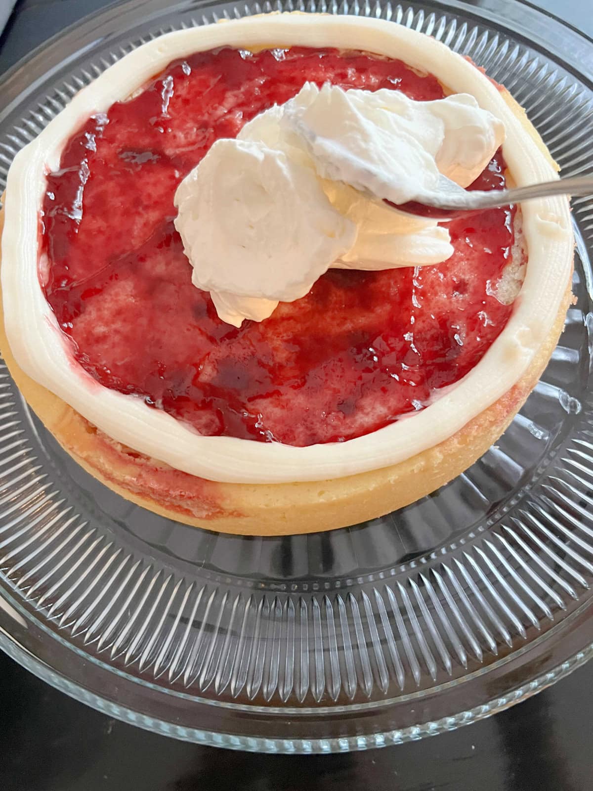 Adding filling of raspberry jam and whipped cream to the cake.