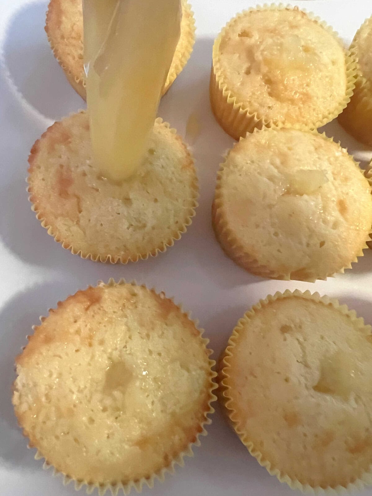 Filling the cupcakes using a disposable piping bag with pineapple filling.