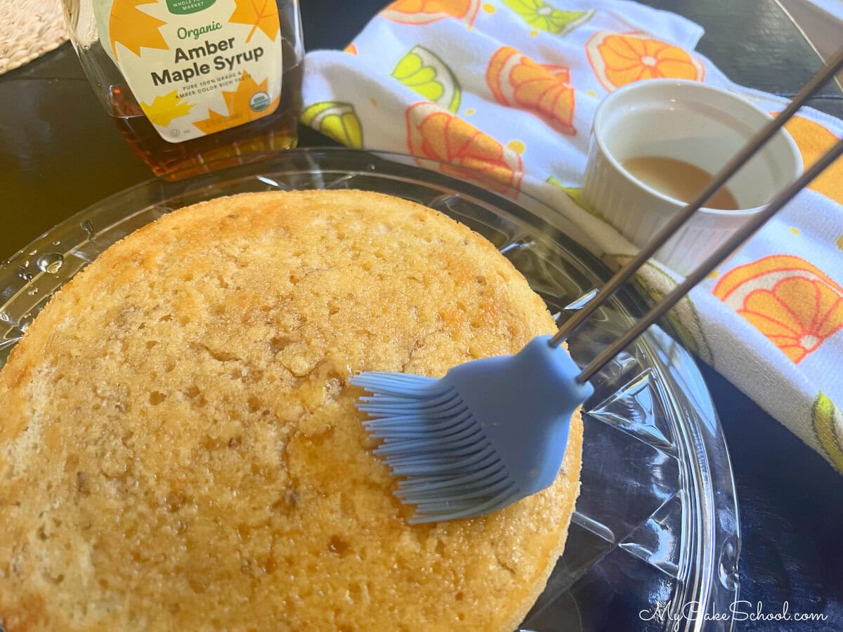 Brushing cake layer with maple syrup.