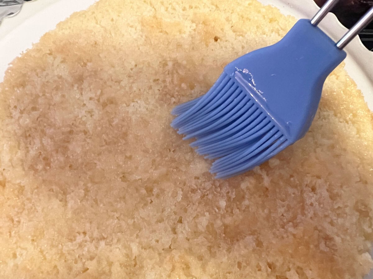 Brushing the top of the cake layer with champagne syrup.