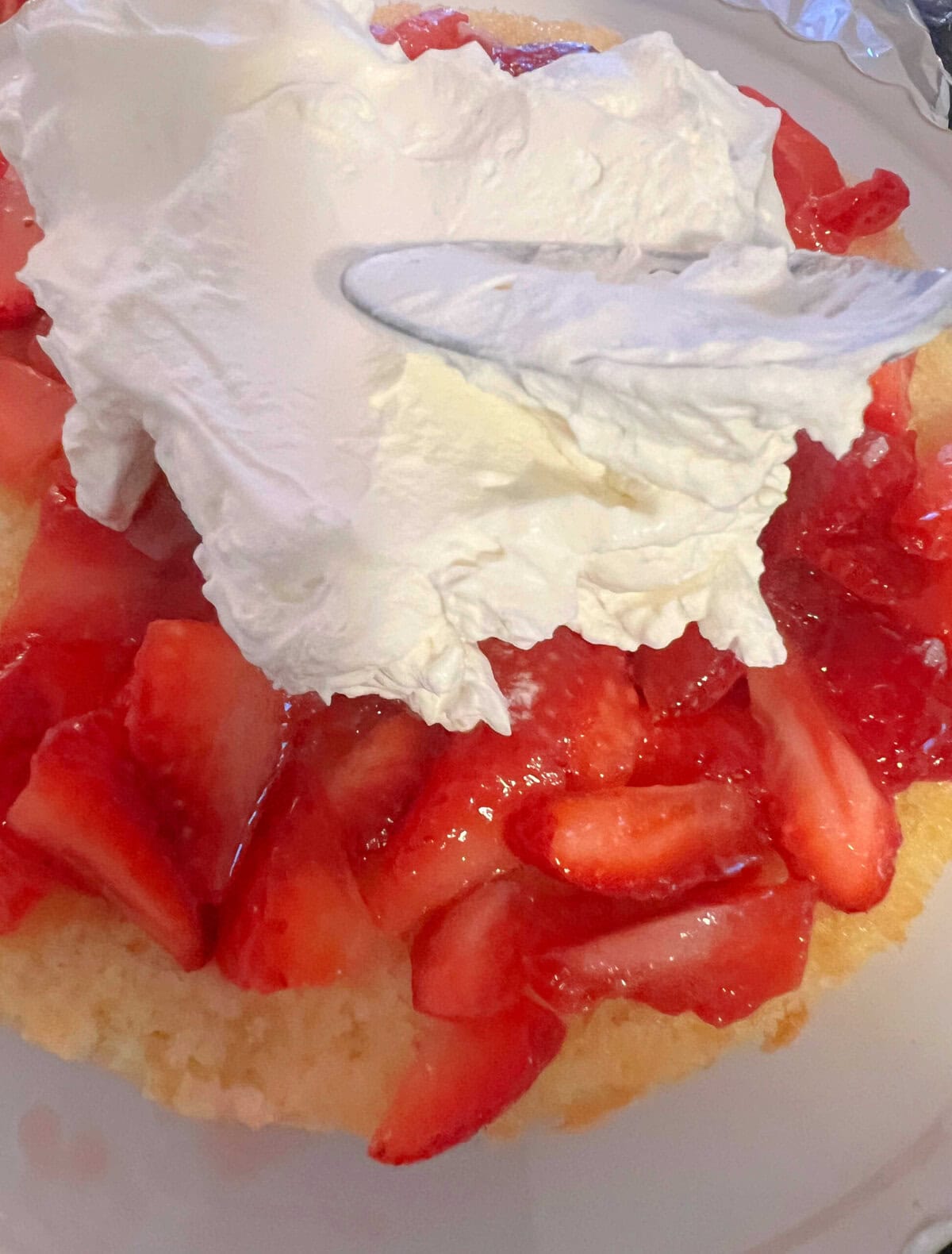 Spreading Whipped Cream over Strawberries on cake layer.