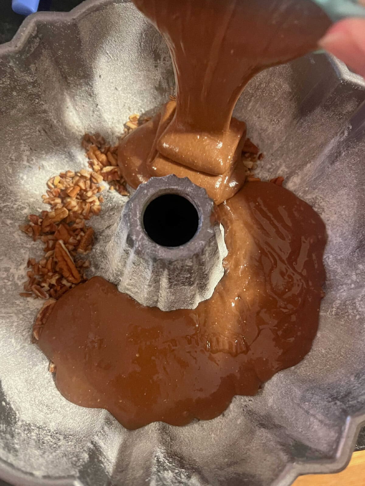 Scooping the batter into the bundt cake, over the chopped pecans.