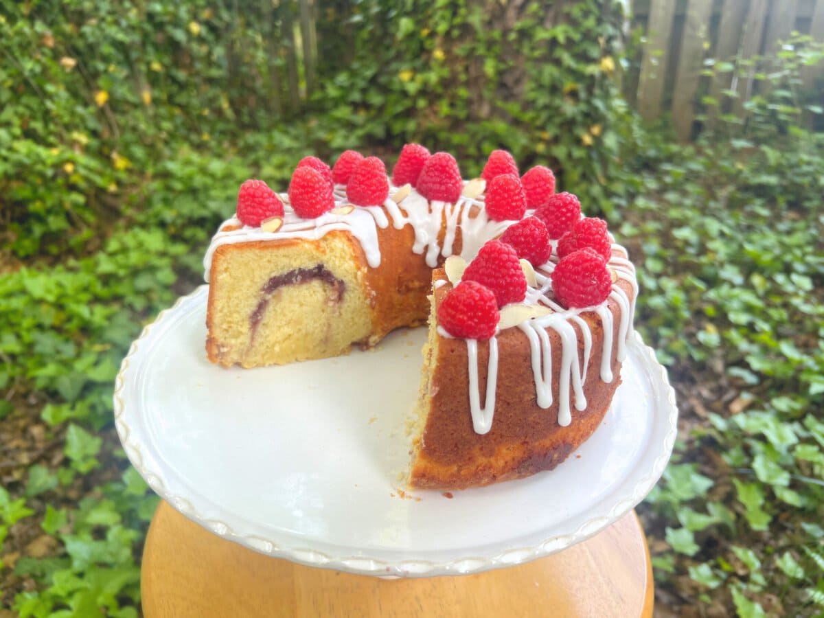 Raspberry Almond Layer Cake, sliced, on a cake pedestal.