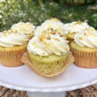 Moist Pistachio Cupcakes on a cake pedestal, swirled with cream cheese frosting.