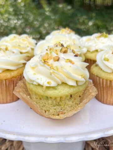 Moist Pistachio Cupcakes on a cake pedestal, swirled with cream cheese frosting.
