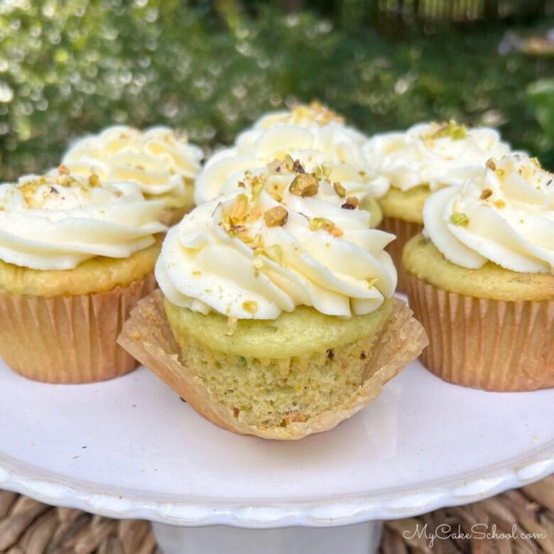 Moist Pistachio Cupcakes on a cake pedestal, swirled with cream cheese frosting.